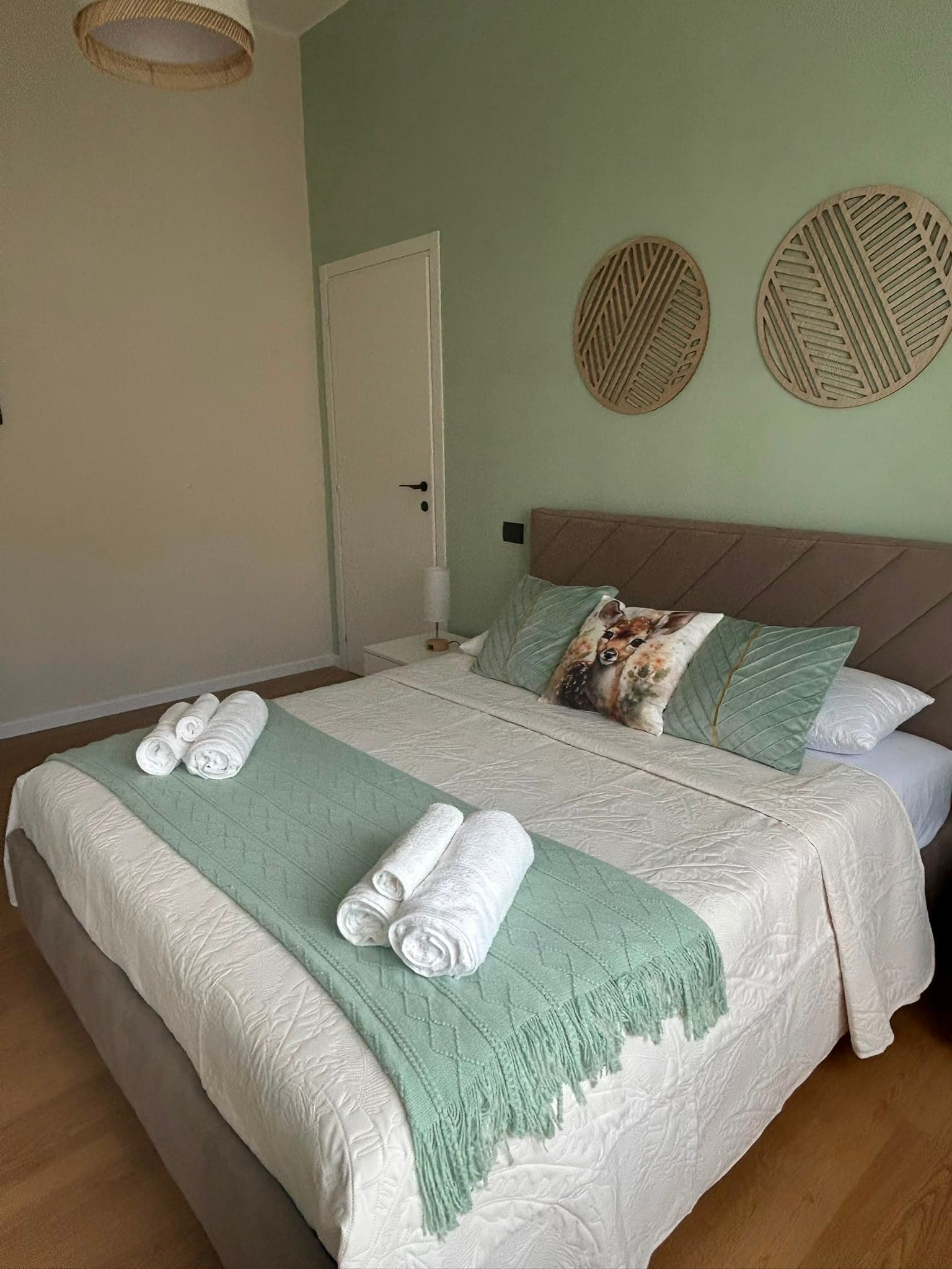 The bedroom at Mari's Home: sage-green cushions and rolled towels on the bed